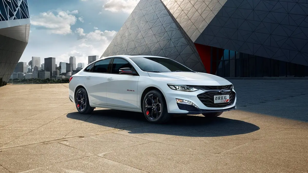 Chevrolet Malibu XL из Китая под заказ — белый седан, вид спереди в три четверти у здания